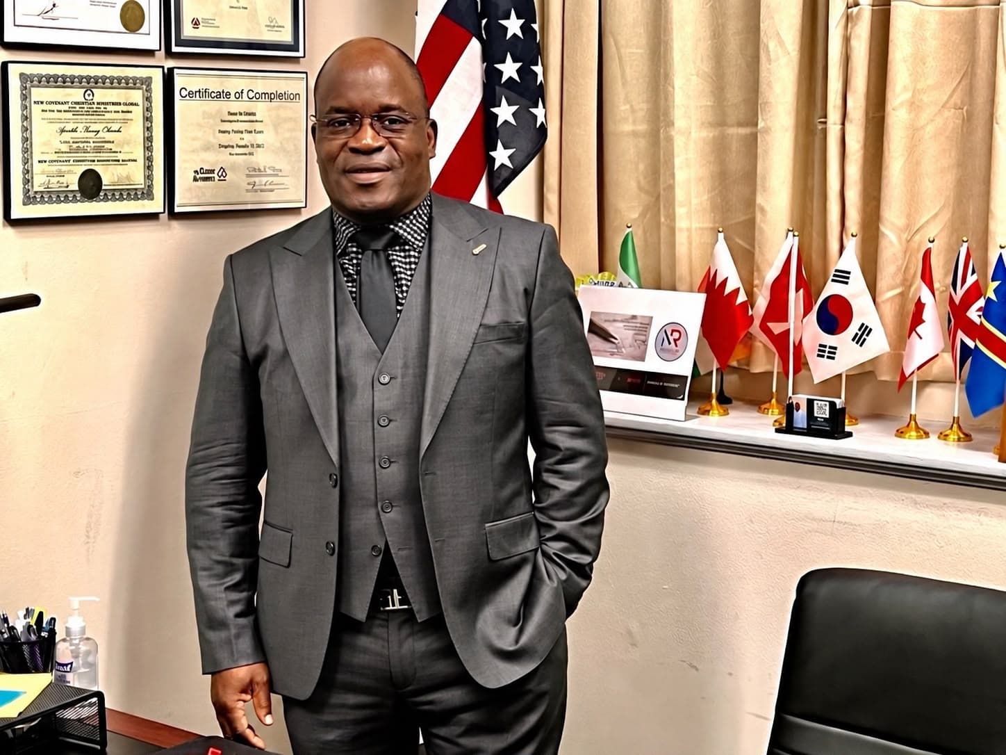 Remy W. OLEMBO, founder of BCR, standing in his office in front of flags, including those of the United States and the DR Congo